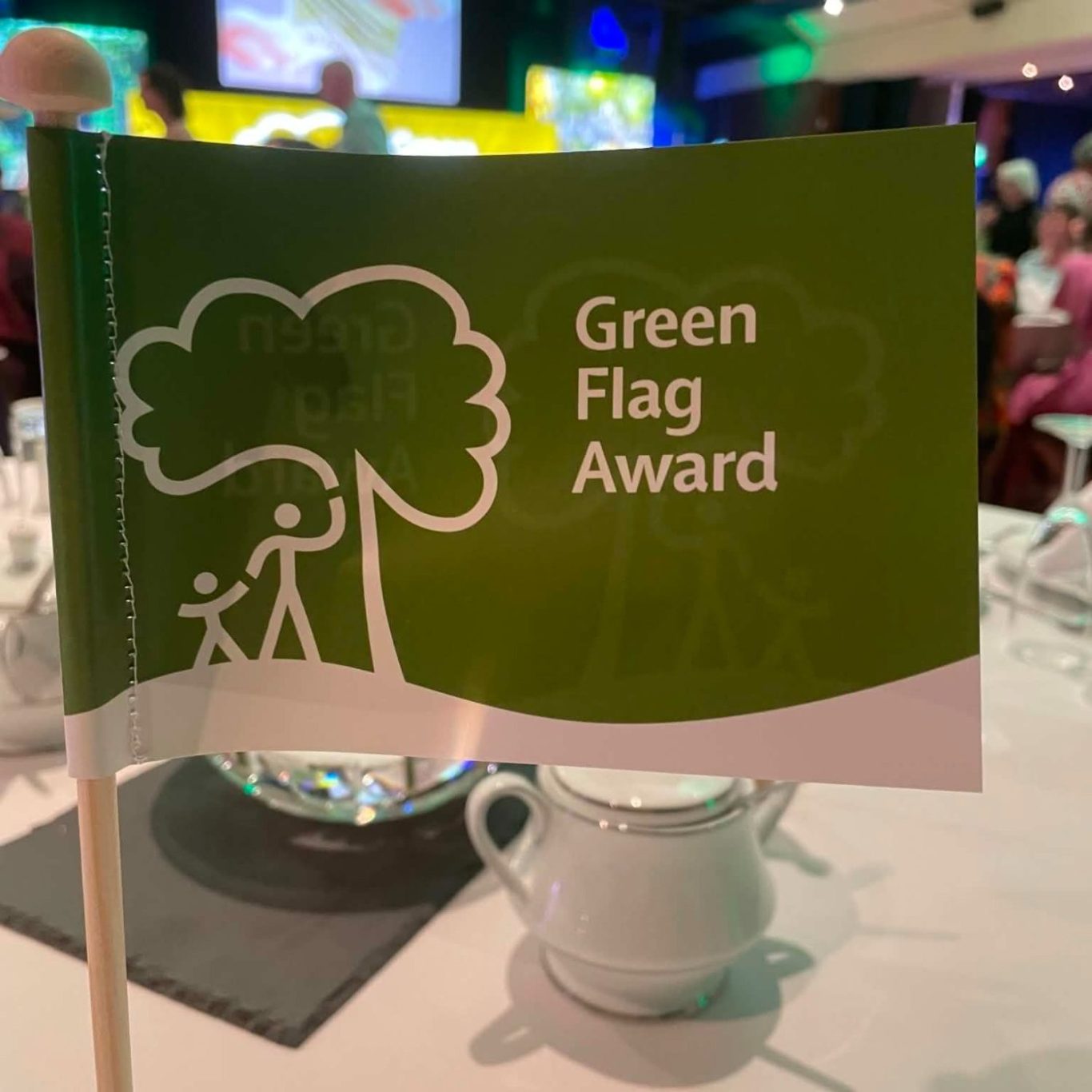 A woman holds a Green Flag Award sign at an event backdrop with trees.
